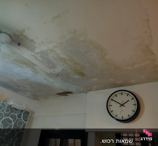 תקרה עם כתמי רטיבות ונזילות ליד מנורה ושעון קיר